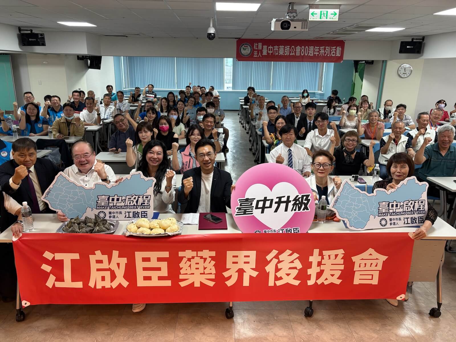 「江啟臣藥界後援會」成立大會現場大合照，桌上擺放象徵「包中」的包子與粽子