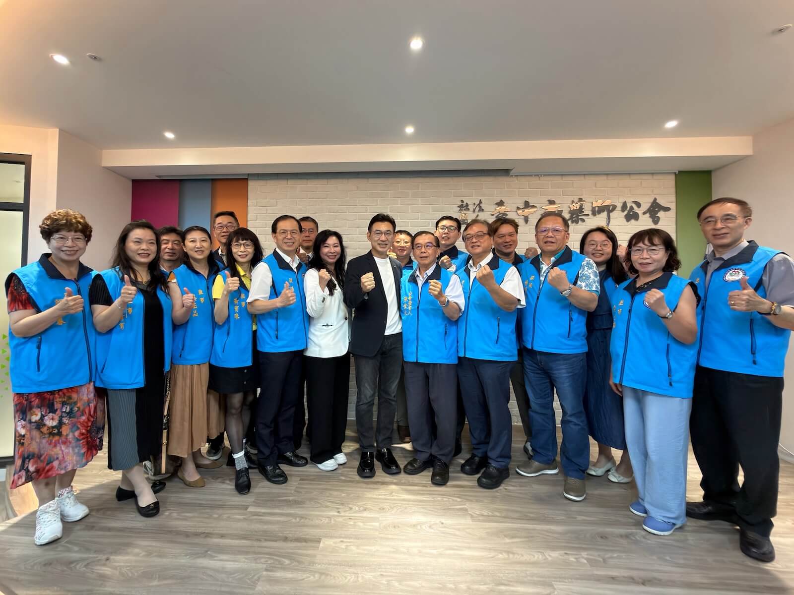 江啟臣與臺中市藥師公會幹部於公會會址前合影，眾人比出加油手勢