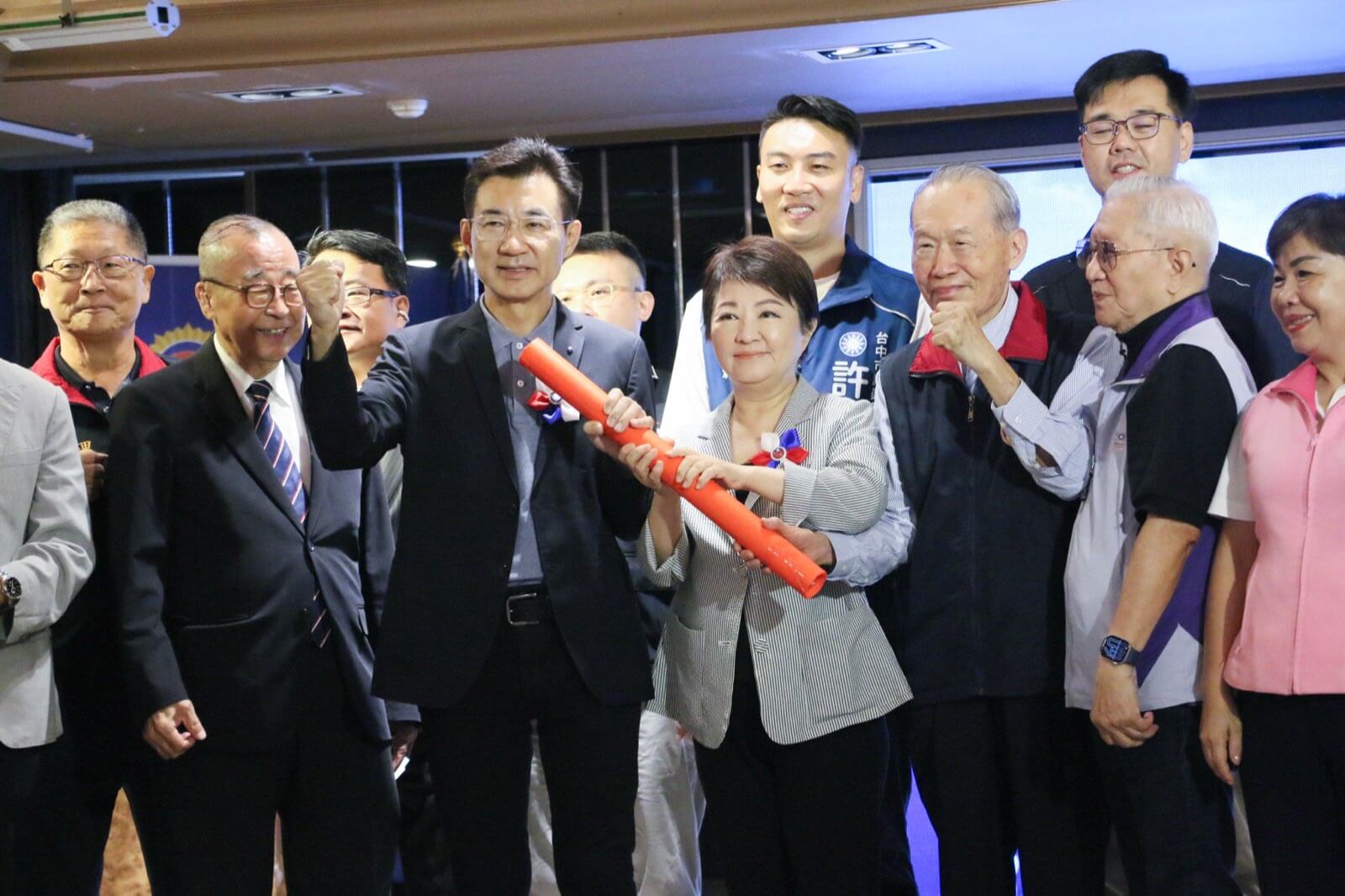 盧秀燕與江啟臣共同握住紅色接力棒，象徵市政交棒，與會來賓在旁舉拳合影
