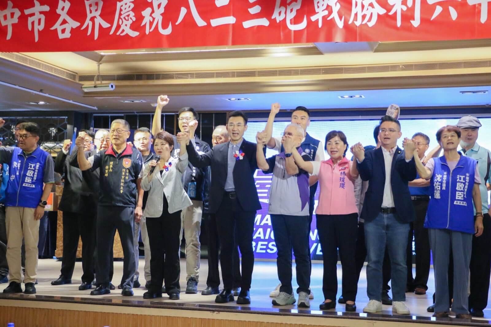 八二三砲戰勝利六十八週年大會會場，江啟臣、盧秀燕與出席來賓在紅布條前牽手高舉呼喊口號