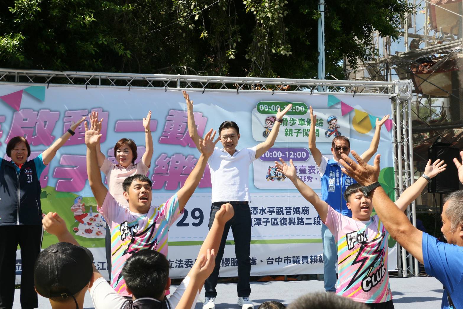 江啟臣站在親子歡樂城舞台中央跟著帶動跳高舉雙手，台下親子一同伸手同樂