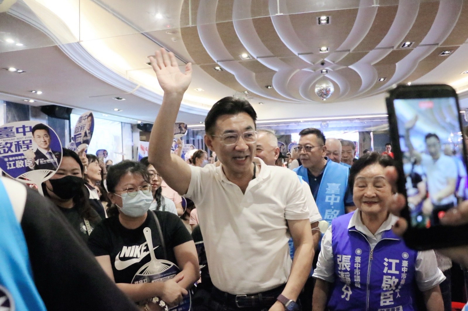 江啟臣走進會場走道向支持者揮手致意，現場民眾舉起手機與宣傳扇迎接