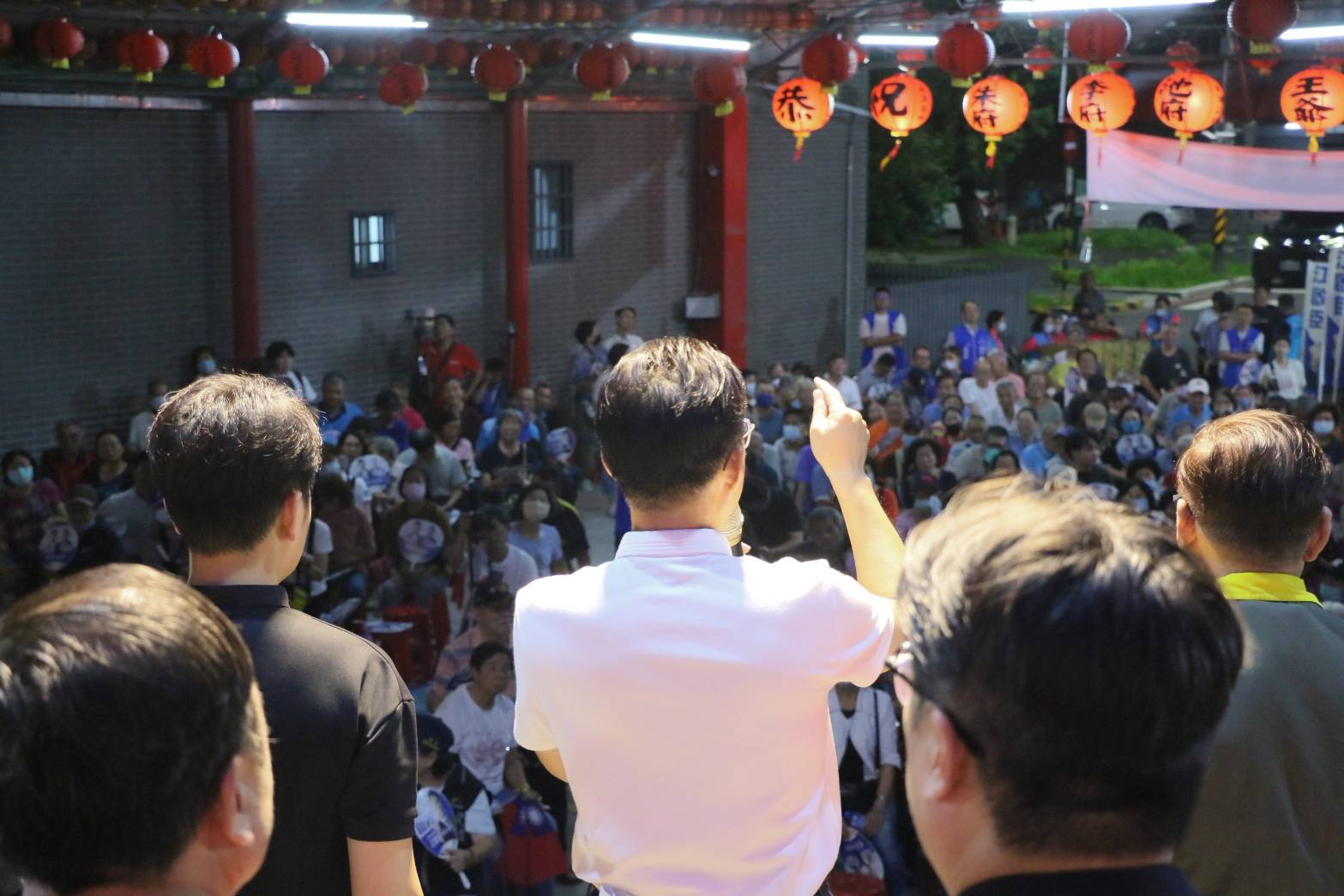 江啟臣站在均安宮廟埕舞台上舉手向台下群眾致詞，頭頂懸掛成排紅色燈籠