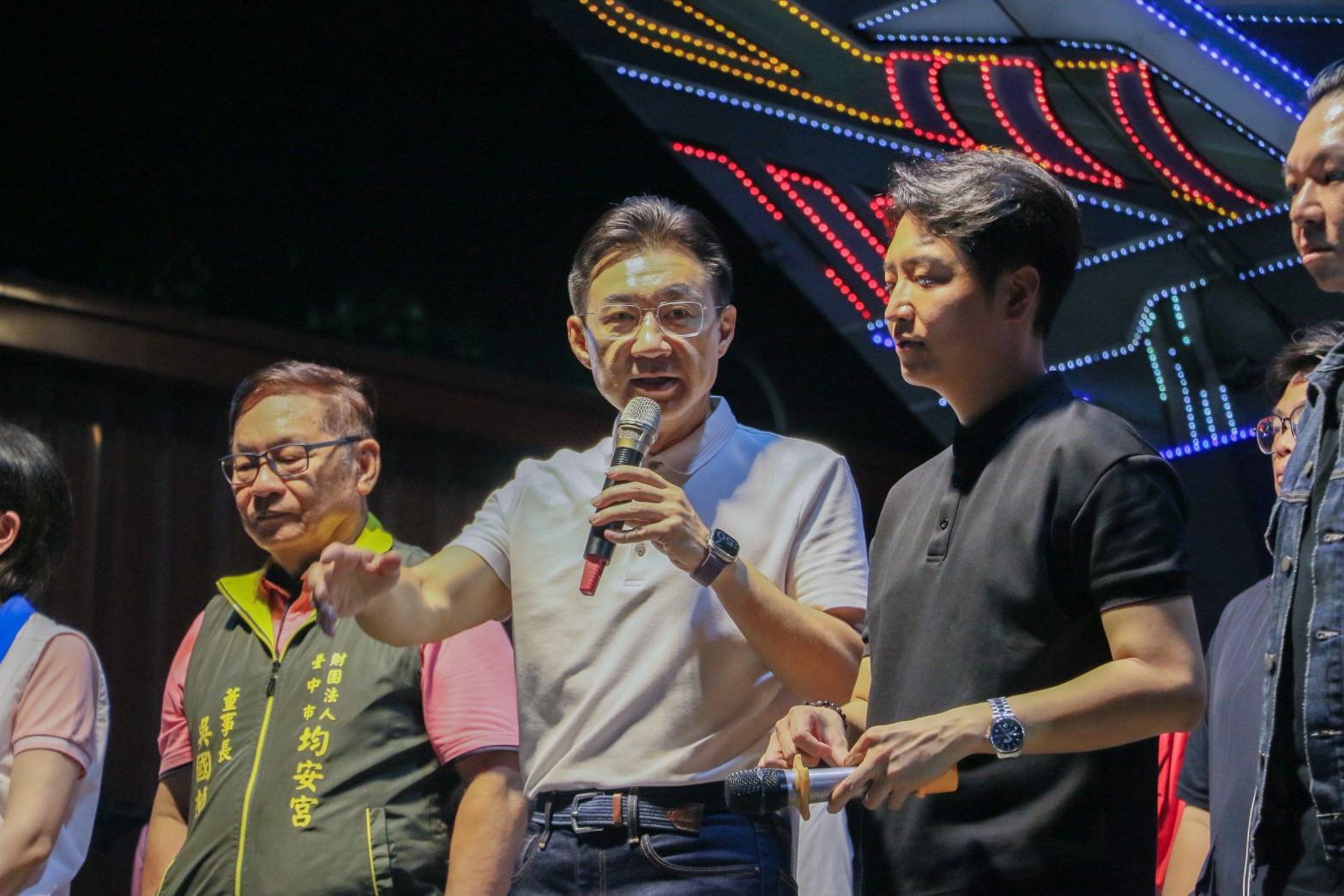 江啟臣在均安宮說明會舞台上持麥克風說明政見，均安宮董事長吳國楨與羅廷瑋在旁聆聽