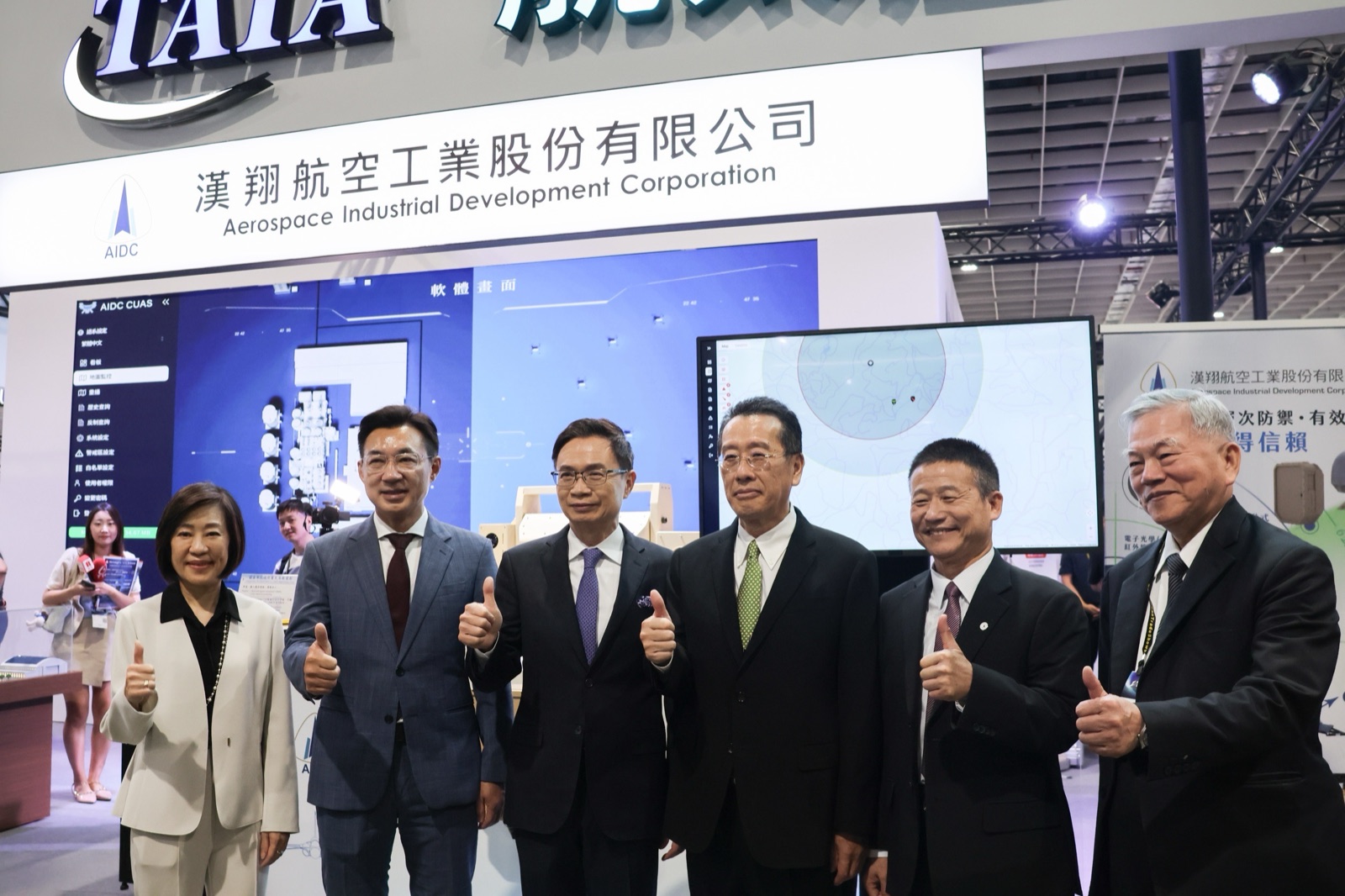 江啟臣在漢翔航空工業展示攤位前與來賓合影，背後為AIDC反無人機系統展示畫面