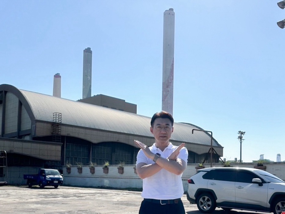 江啟臣站在臺中火力發電廠煙囪前，雙手交叉比出拒絕手勢