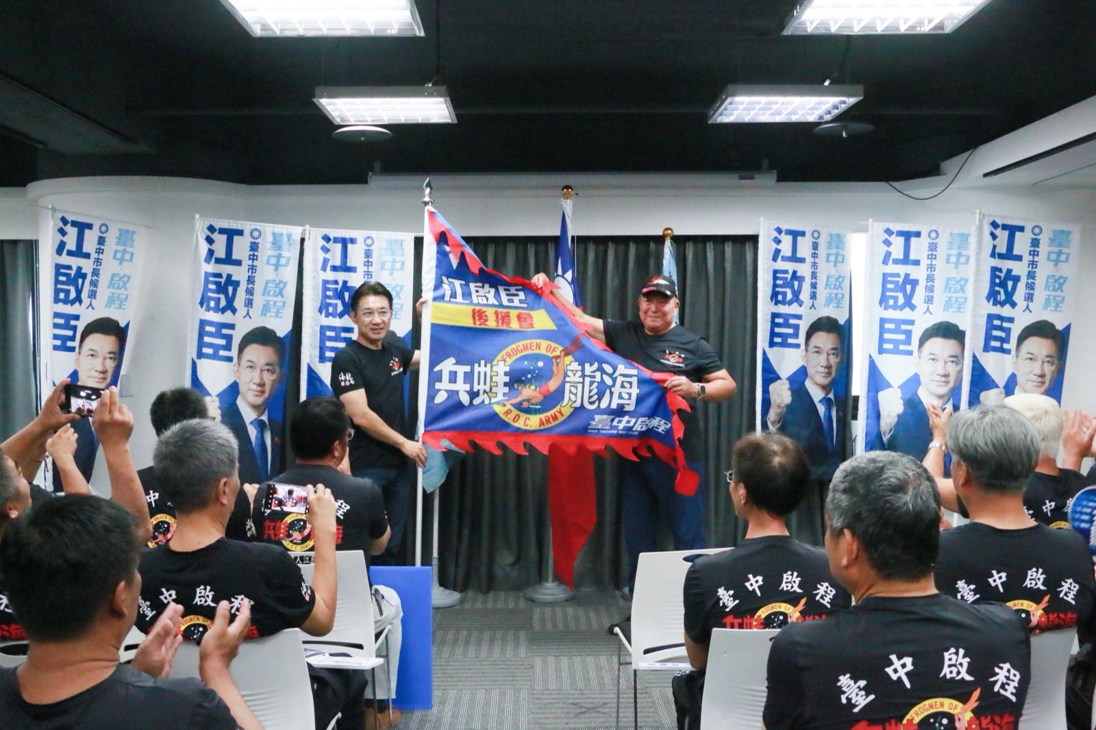 江啟臣與後援會會長在台上共同展開「兵蛙龍海」後援會會旗，台下弟兄鼓掌
