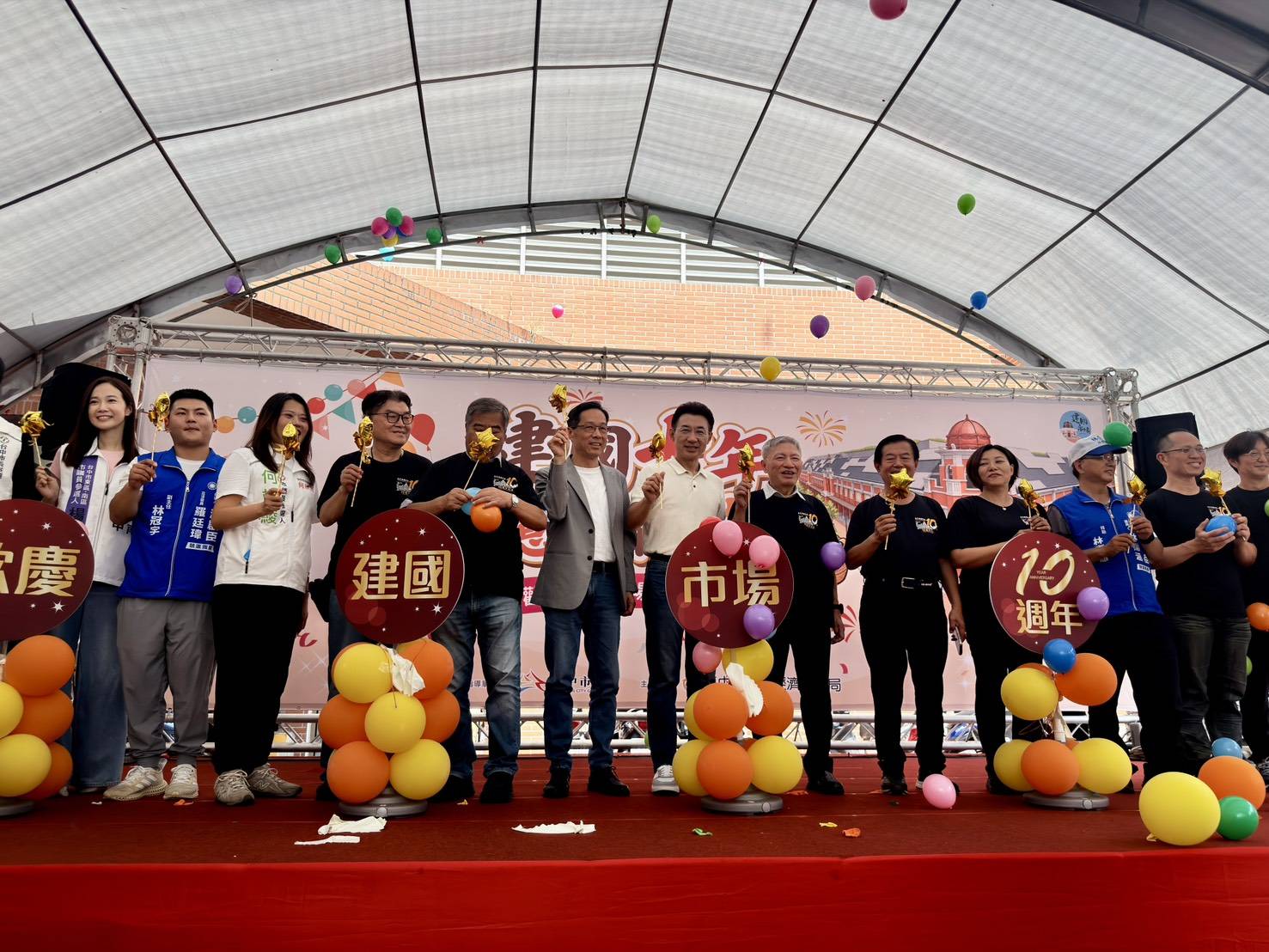 建國市場遷建十週年慶祝活動舞台上，江啟臣與貴賓手持星星棒，在「建國市場10週年」氣球立牌旁共同歡慶