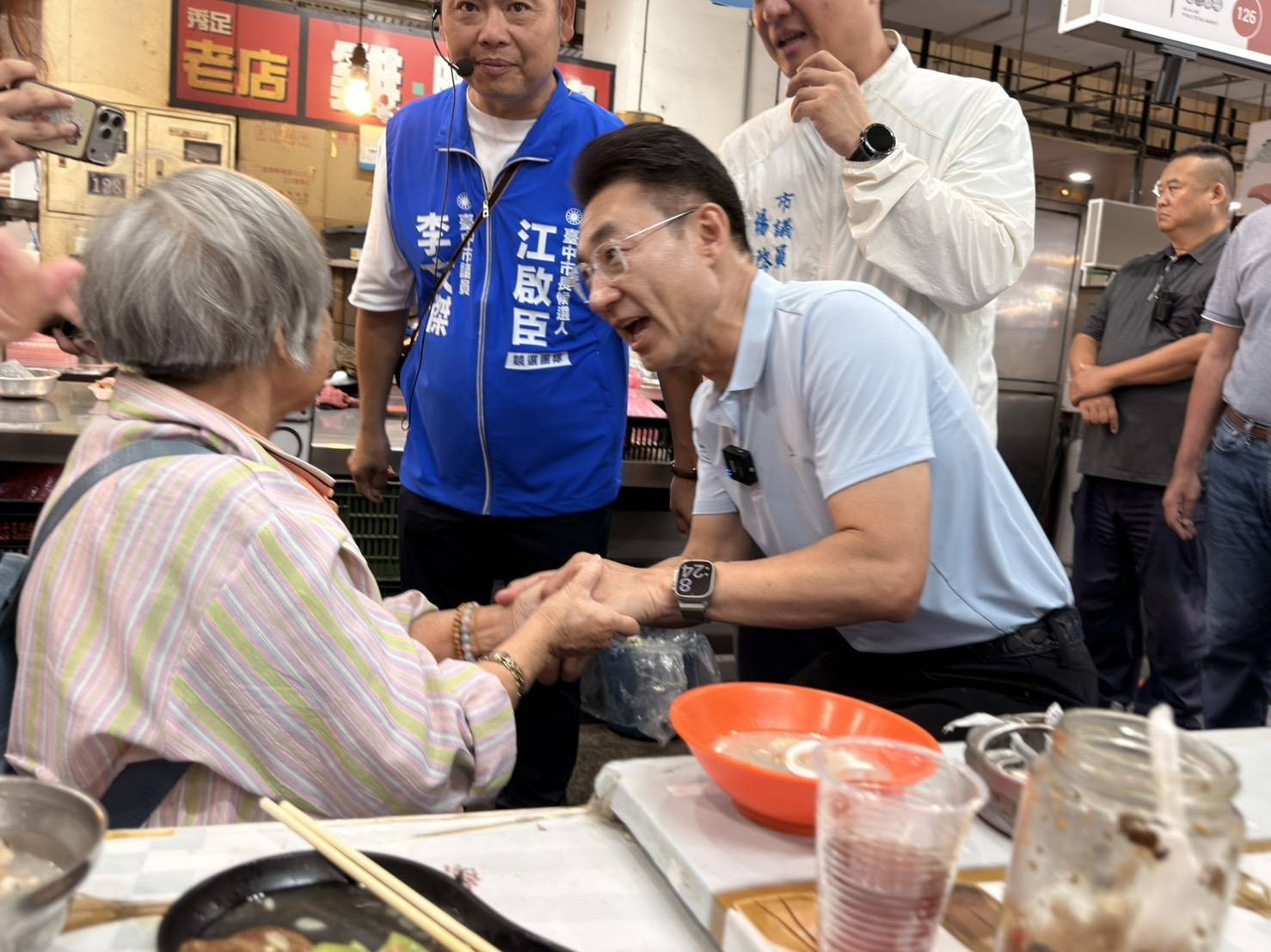 市場點心攤前，江啟臣彎身與一位長輩握手問候，市議員李文傑在旁