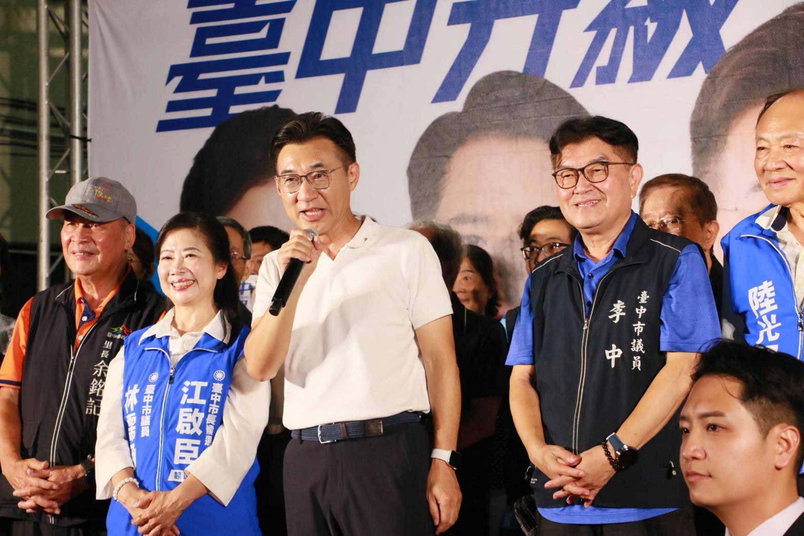 江啟臣持麥克風在台上致詞，市議員林霈涵、李中在旁聆聽