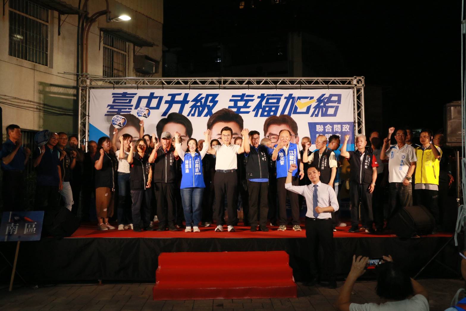 「臺中升級 幸福加給」聯合問政說明會舞台全景，江啟臣與民代、里長一字排開高舉手臂