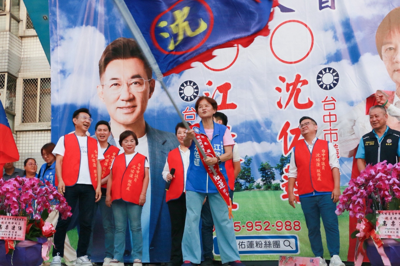 議員沈佑蓮揮舞競選旗幟，江啟臣與同台來賓穿著「沈佑蓮服務處」紅色背心站在一旁
