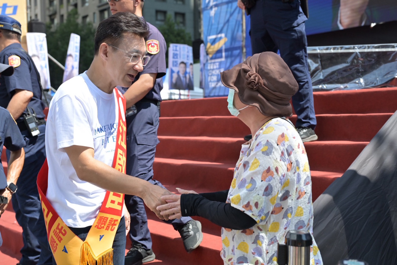 江啟臣披著「江啟臣」肩帶，在舞台階梯旁與一位鄉親握手致意