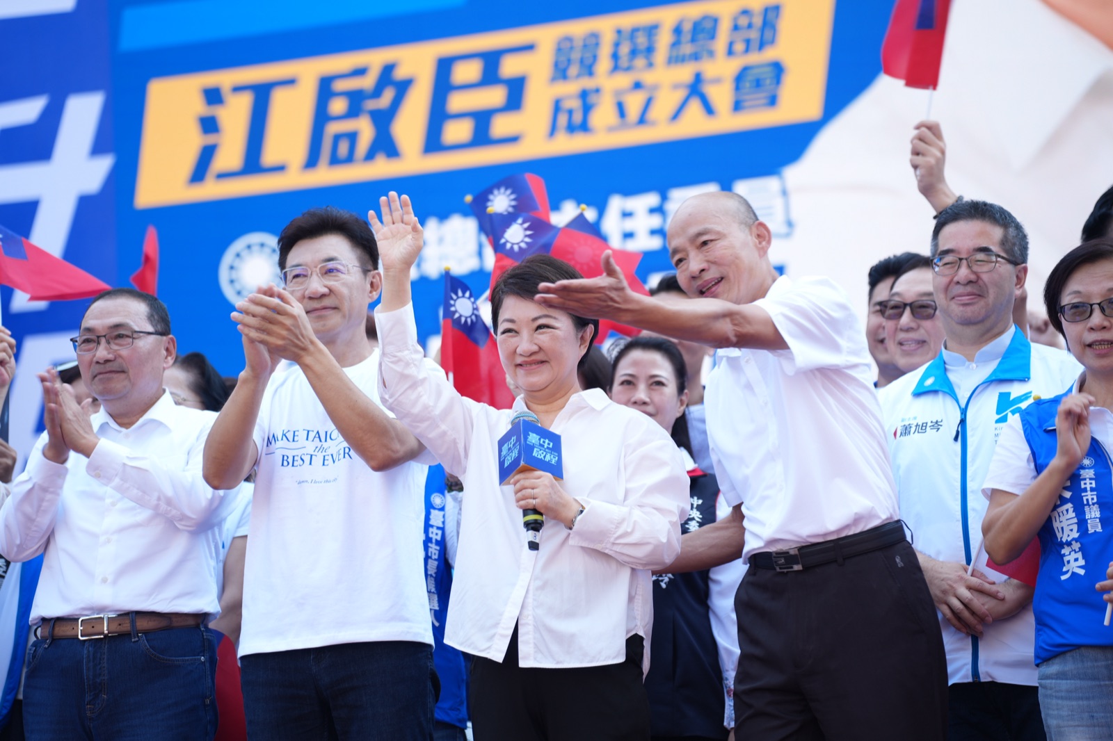 江啟臣與台上來賓鼓掌歡呼，背板寫著「江啟臣競選總部成立大會」