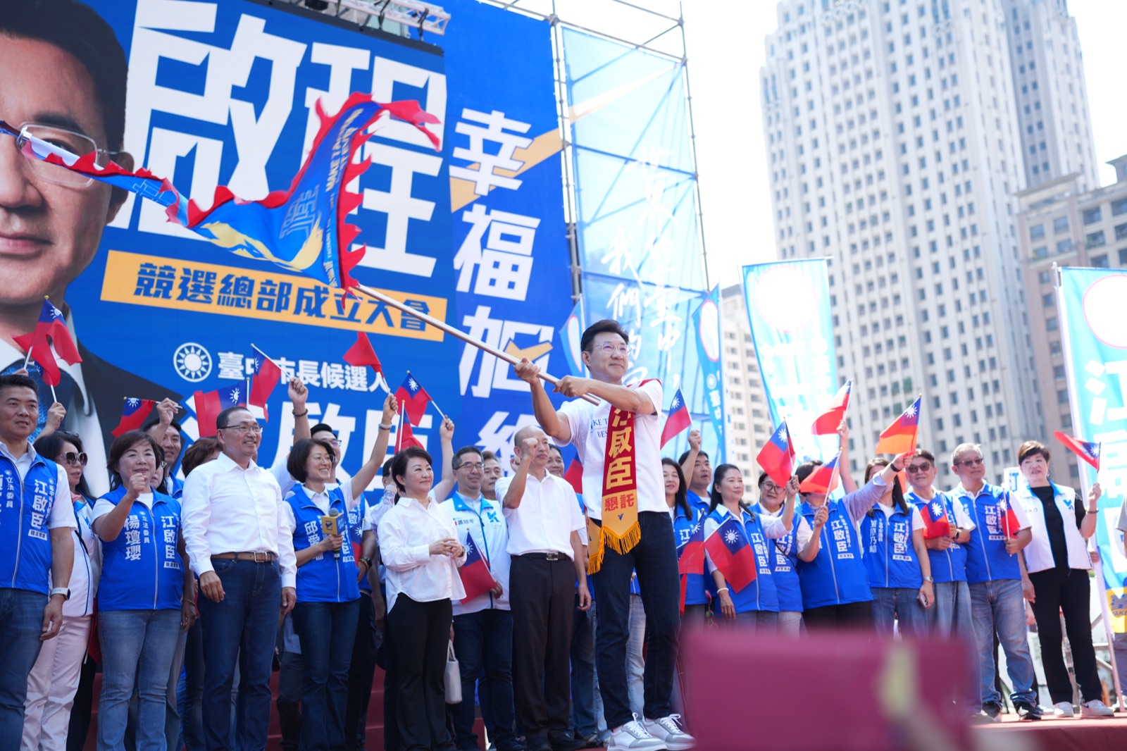 江啟臣披著肩帶，在台上揮舞大旗，身後眾人揮舞國旗