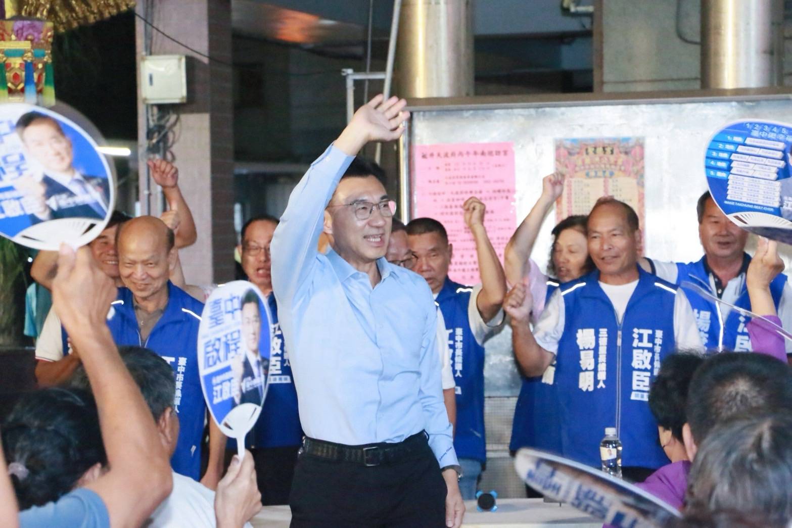 江啟臣在聖德宮揮手向鄉親致意，身後穿「江啟臣」背心的支持者握拳歡呼，其中一件背心寫著三德里楊易明