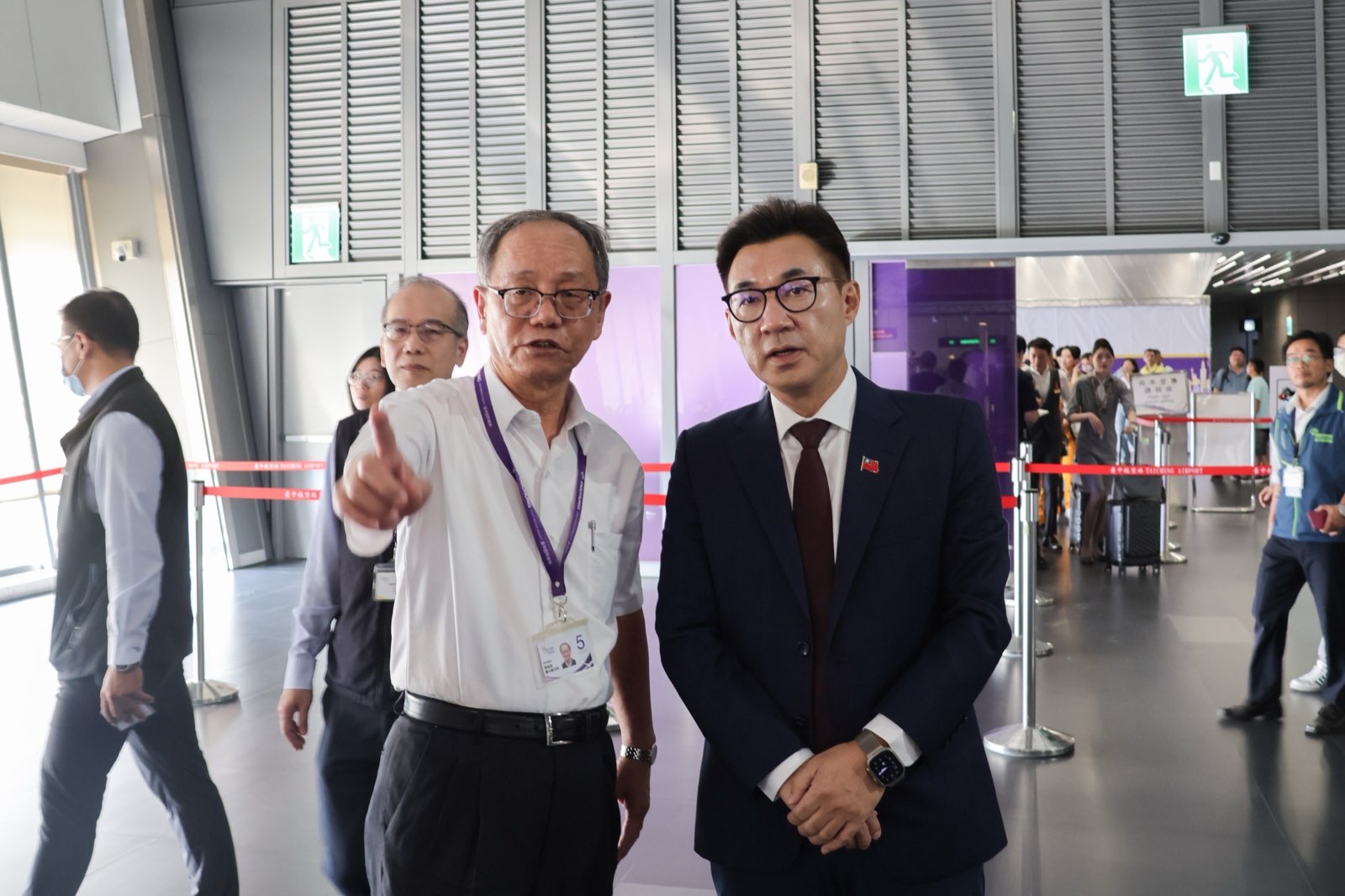江啟臣在臺中國際機場航廈內聽取機場人員說明，背景可見旅客排隊候機