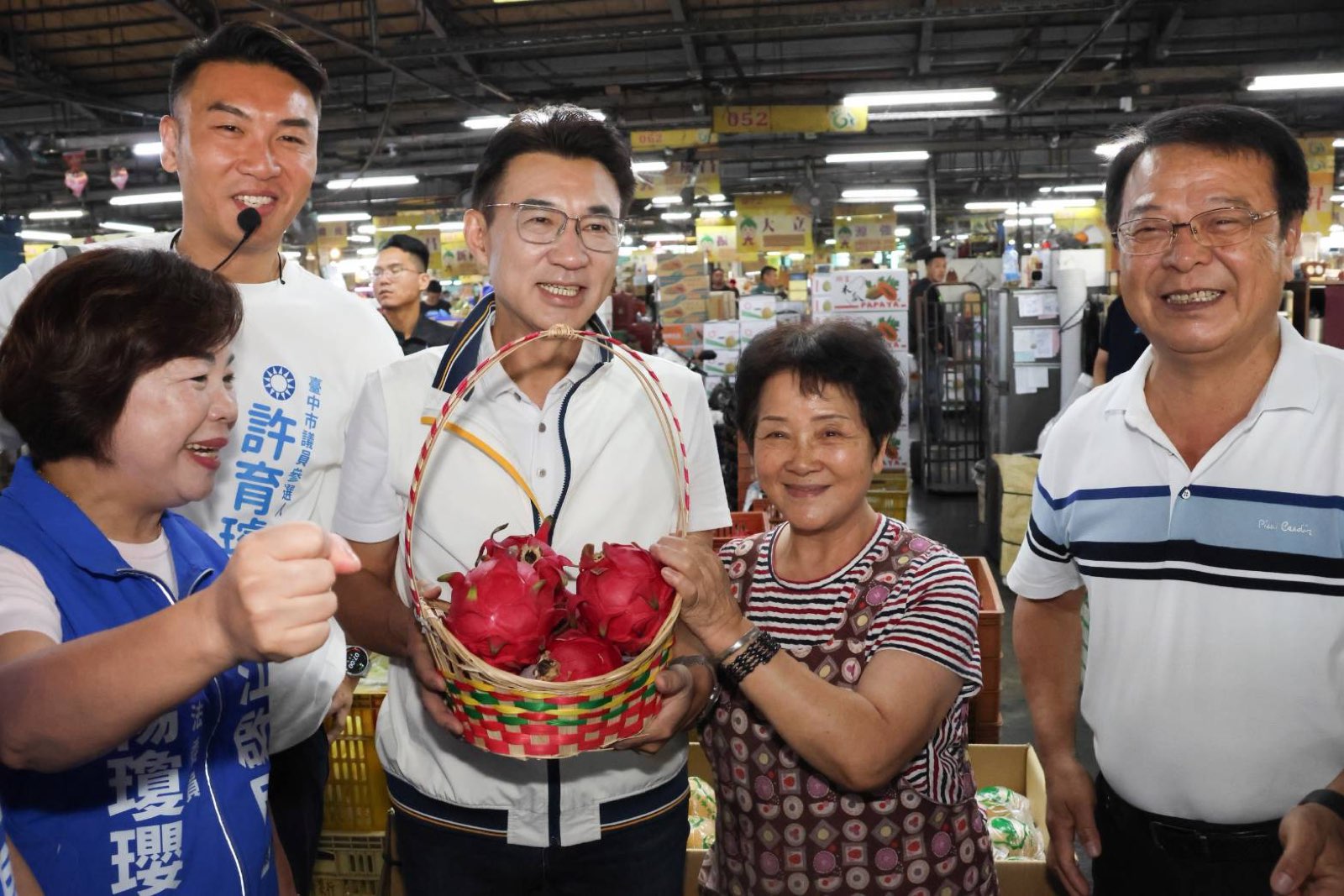 江啟臣在臺中果菜市場手捧攤商送上的紅龍果禮籃，楊瓊瓔、市議員參選人許育璿在旁合影
