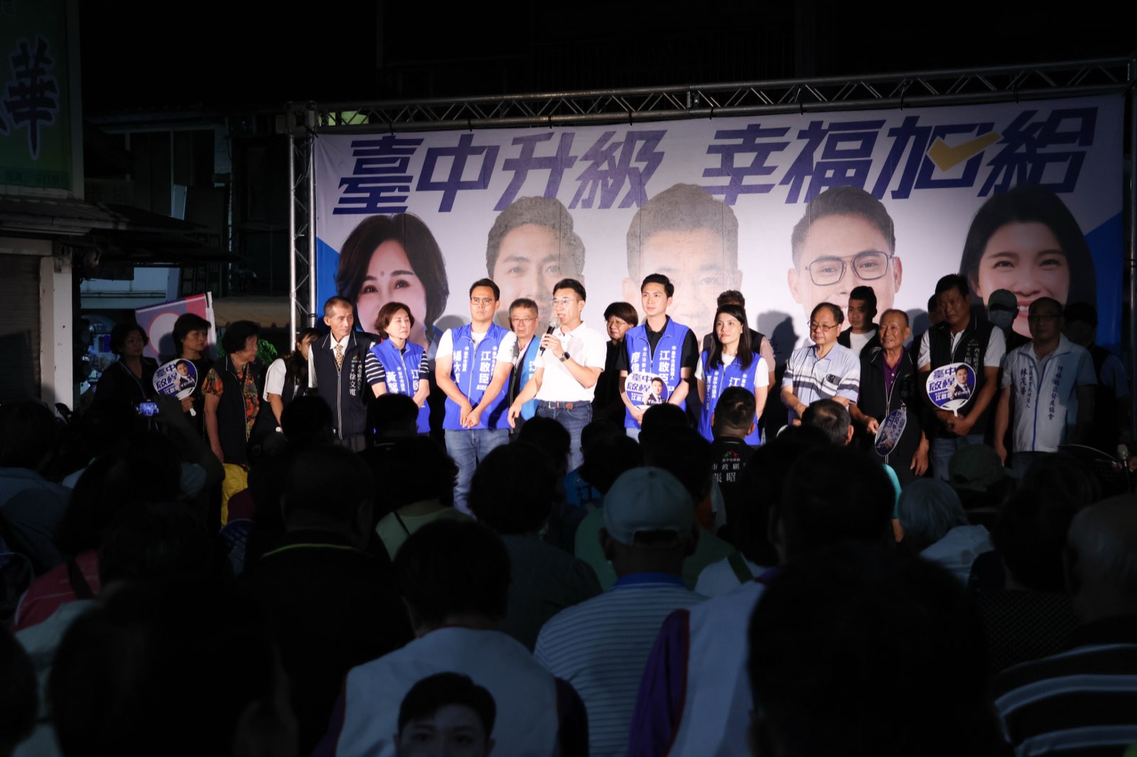 「臺中升級、幸福加給」西屯說明會舞台全景，江啟臣與民代、里長站在看板前，台下座無虛席