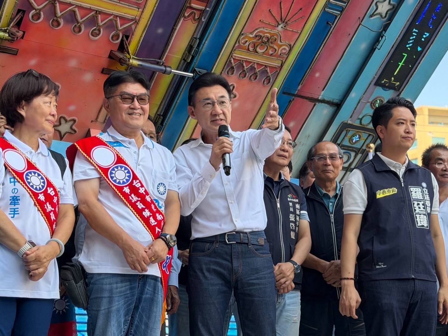 東南區聯合競選總部成立大會，白襯衫男子手持麥克風指向前方發言，左側兩人披「東南區市議員候選人」肩帶，右側穿「立法委員 羅廷瑋」背心的人在一旁聆聽
