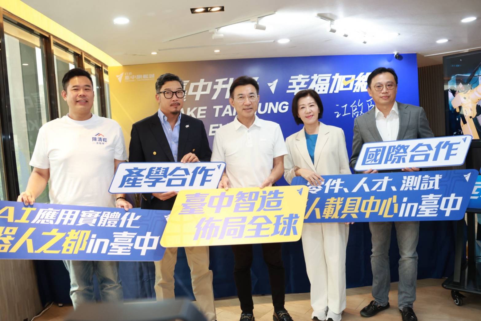 「臺中智造 佈局全球」政策發布記者會合影，五人手持「產學合作」「國際合作」「臺中智造 佈局全球」及機器人之都、無人載具中心等字樣的看板，背後是「臺中升級 幸福加給」背板