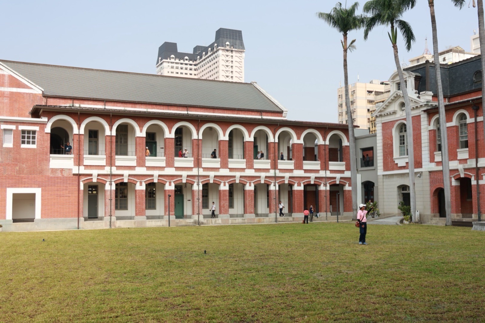 修復後的紅磚拱廊歷史建築與前方草坪，遊客在二樓與廊下參觀，右側可見州廳主樓