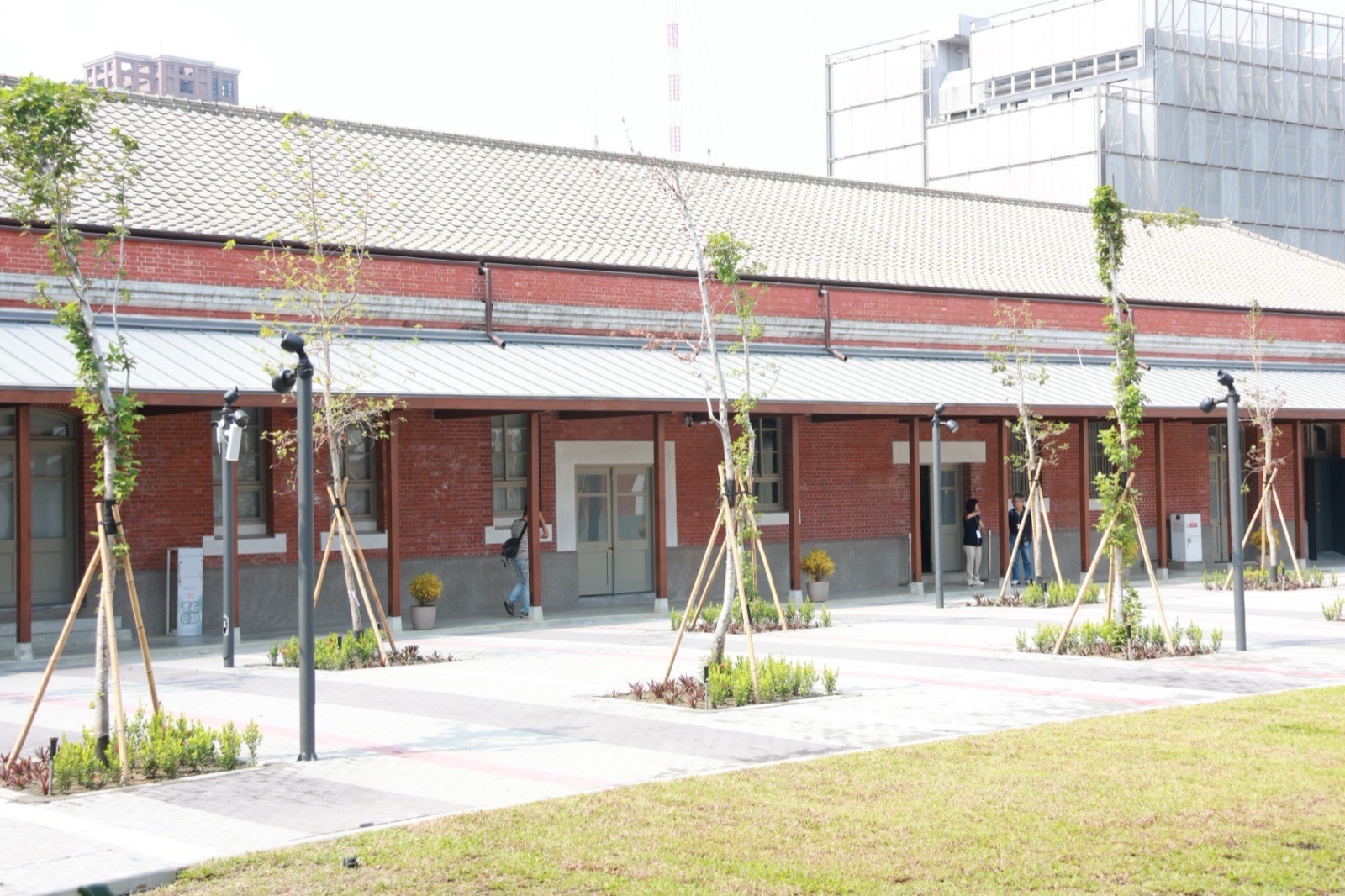 修復後的紅磚歷史建築長廊與鋪面廣場，新植的樹木以竹架支撐