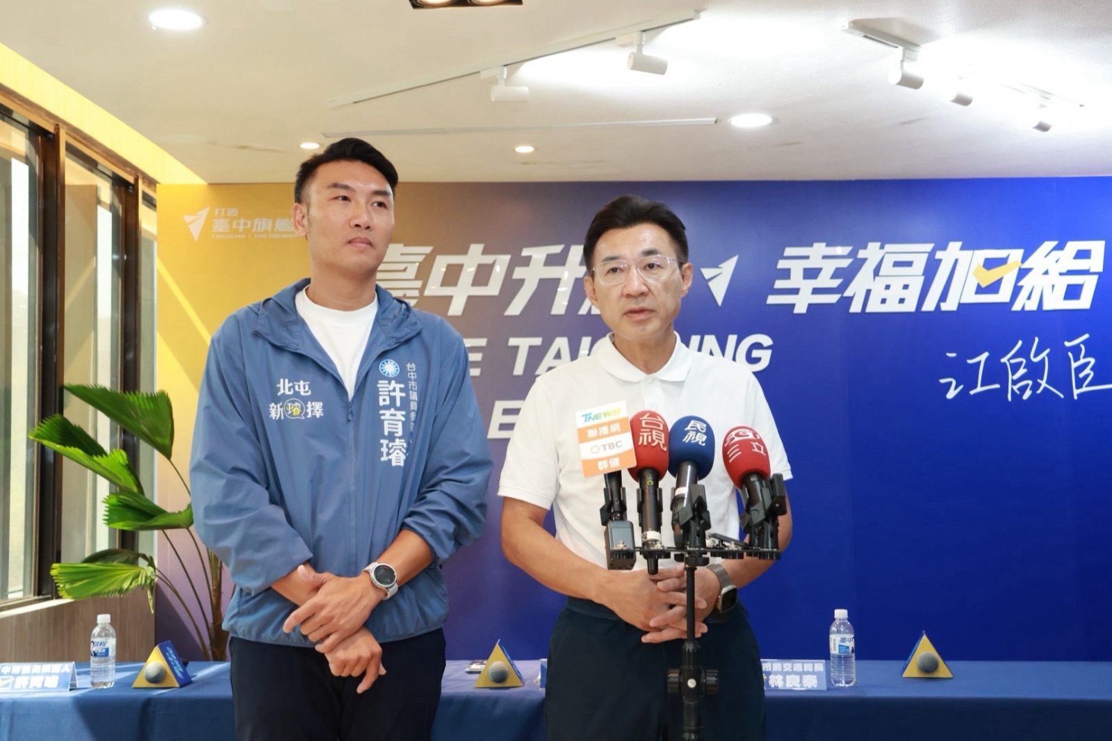 記者會後，穿白色Polo衫的男子面對多家媒體麥克風受訪，左側穿「許育璿」藍外套的男子在旁站立