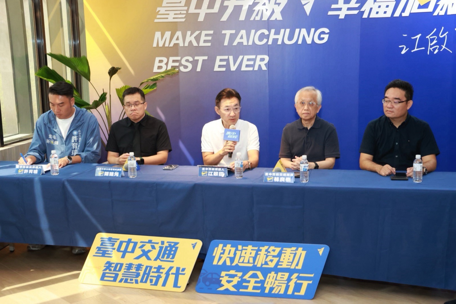 記者會主桌五人並排就座，桌牌依序標示「臺中市議員候選人 許育璿」、「江啟臣」與「臺中市前交通局長 林良泰」等，前方地上擺著「臺中交通 智慧時代」「快速移動 安全暢行」看板