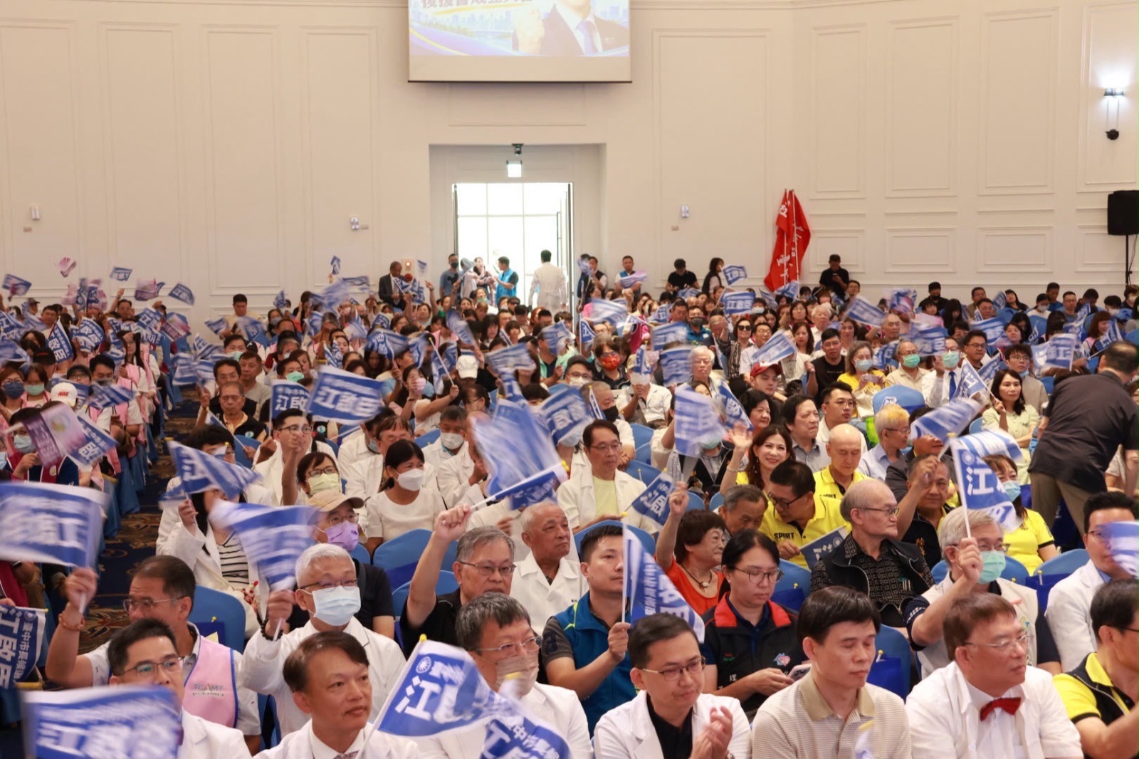 會場座無虛席，與會的醫事、長照界人士揮舞印有「江啟臣」的藍色小旗，其中多人身穿白袍