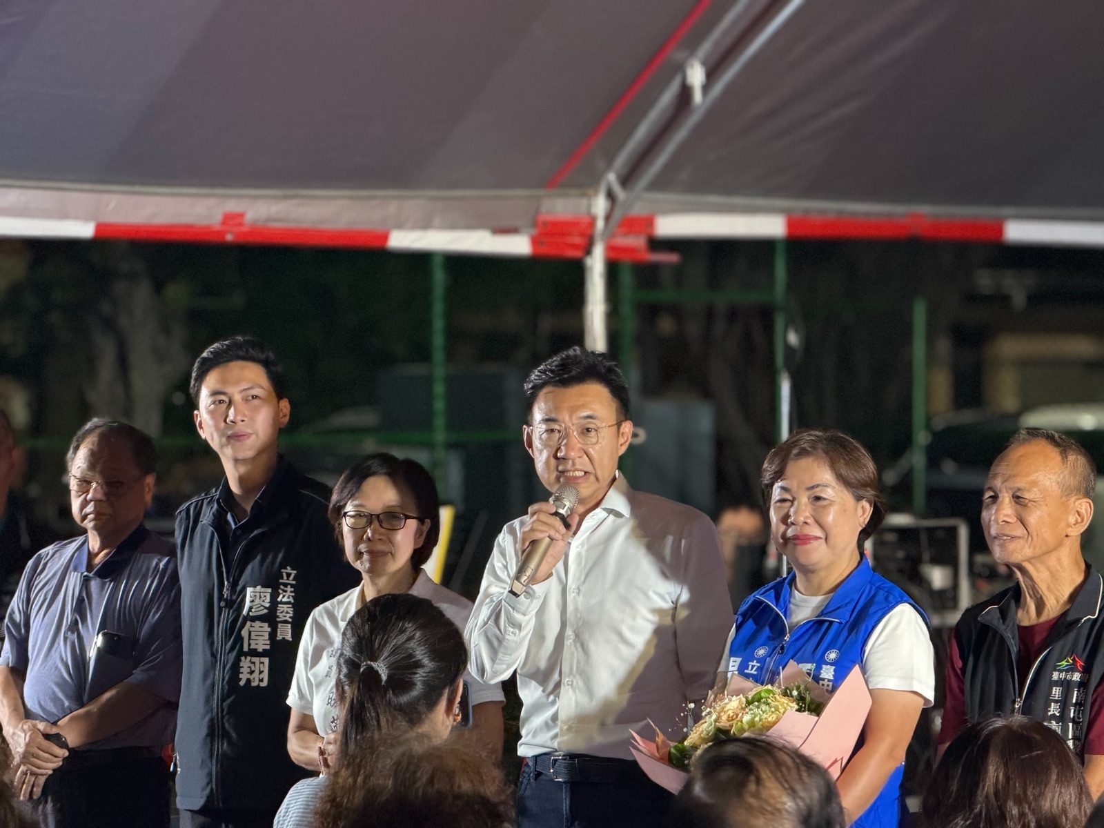 穿白襯衫的男子手持麥克風發言，兩側站著穿「立法委員 廖偉翔」背心的男子、穿藍色背心的女士與南屯區里長