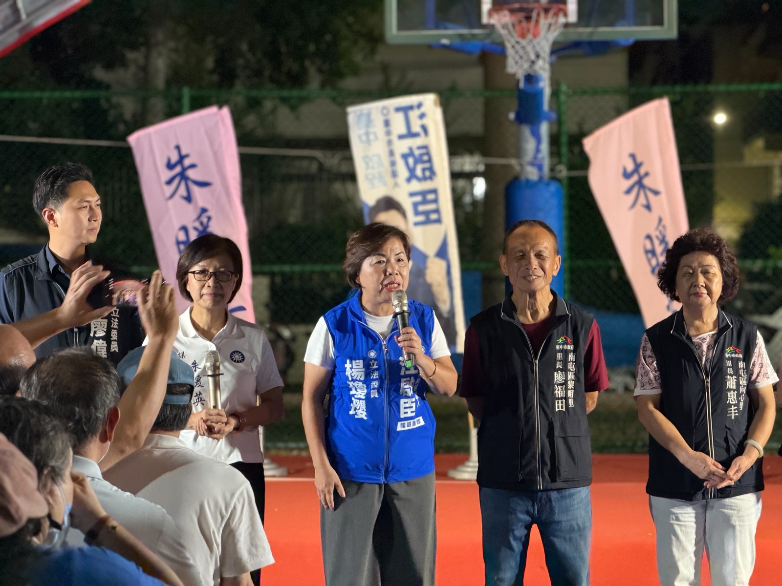 穿藍色「立法委員 楊瓊瓔」背心的女士手持麥克風發言，兩側為廖偉翔立委、朱暖英議員，以及穿「南屯區黎明里 里長 廖福田」「南屯區向心里 里長 蕭惠丰」背心的里長，後方是印有「朱暖英」「江啟臣」的旗幟
