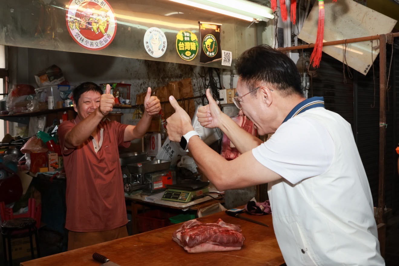 豬肉攤內，穿白色運動外套的男子與攤商雙方各比雙手大拇指，攤商笑得開懷