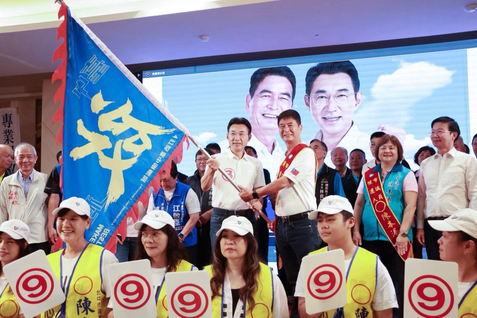 江啟臣在陳本添競選總部成立大會上為市議員陳本添授旗，台前志工高舉9號看板