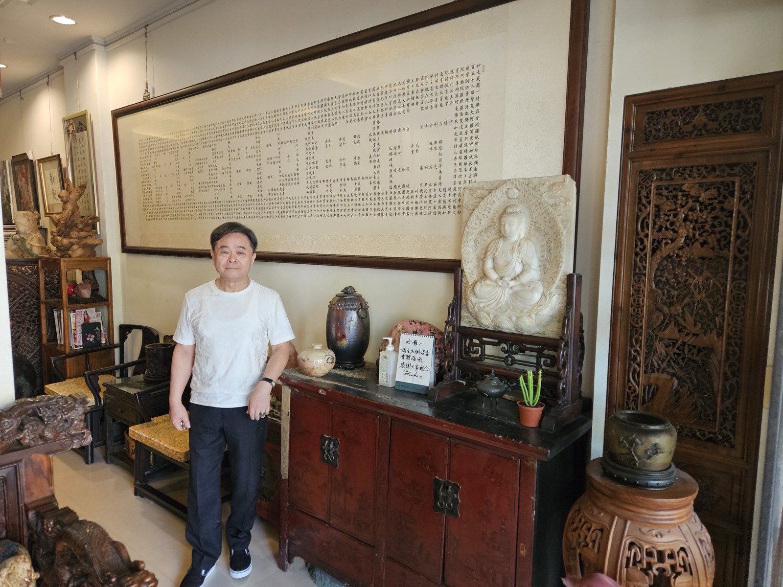 周良敦站在工作室內，身後是一幅以密密麻麻小字排列成大字的書法巨作