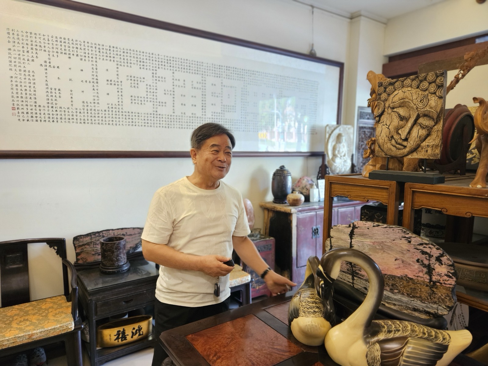 周良敦在工作室中笑著介紹作品，身後牆上掛著一幅由小字排列成大字的長卷書法