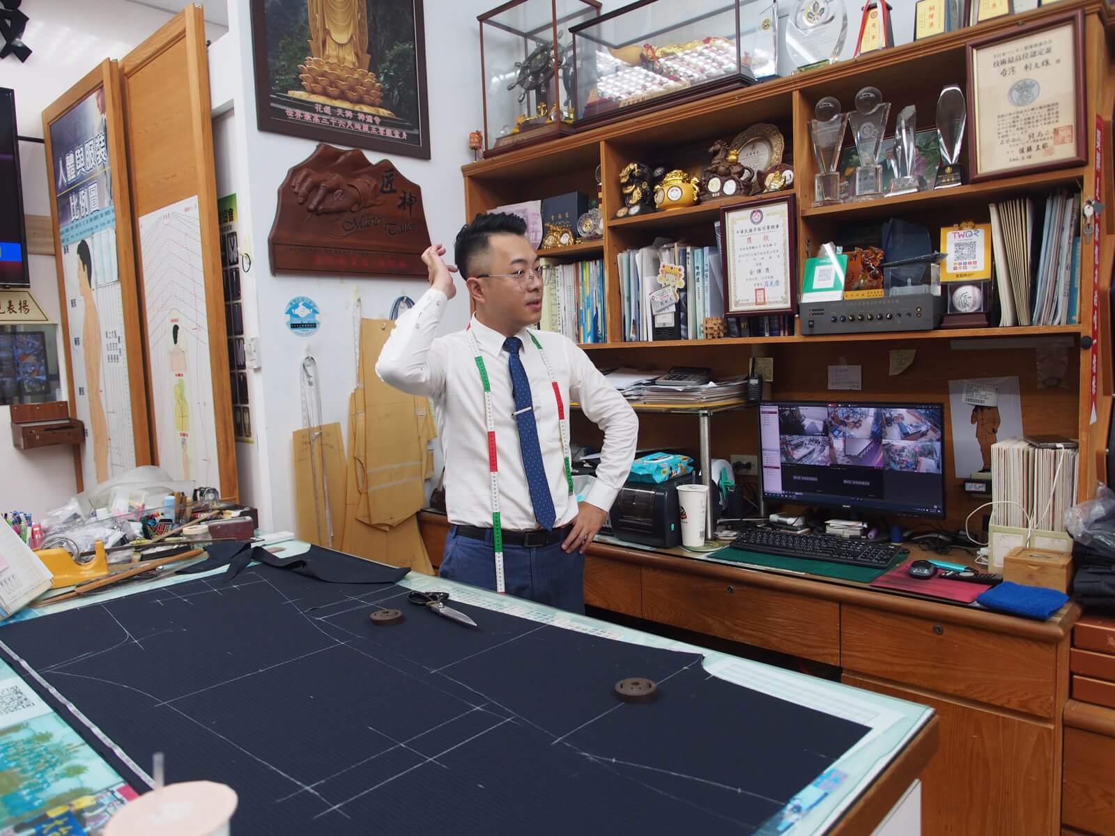 利士杰站在裁剪檯前，桌上鋪著畫好版型記號的深色布料