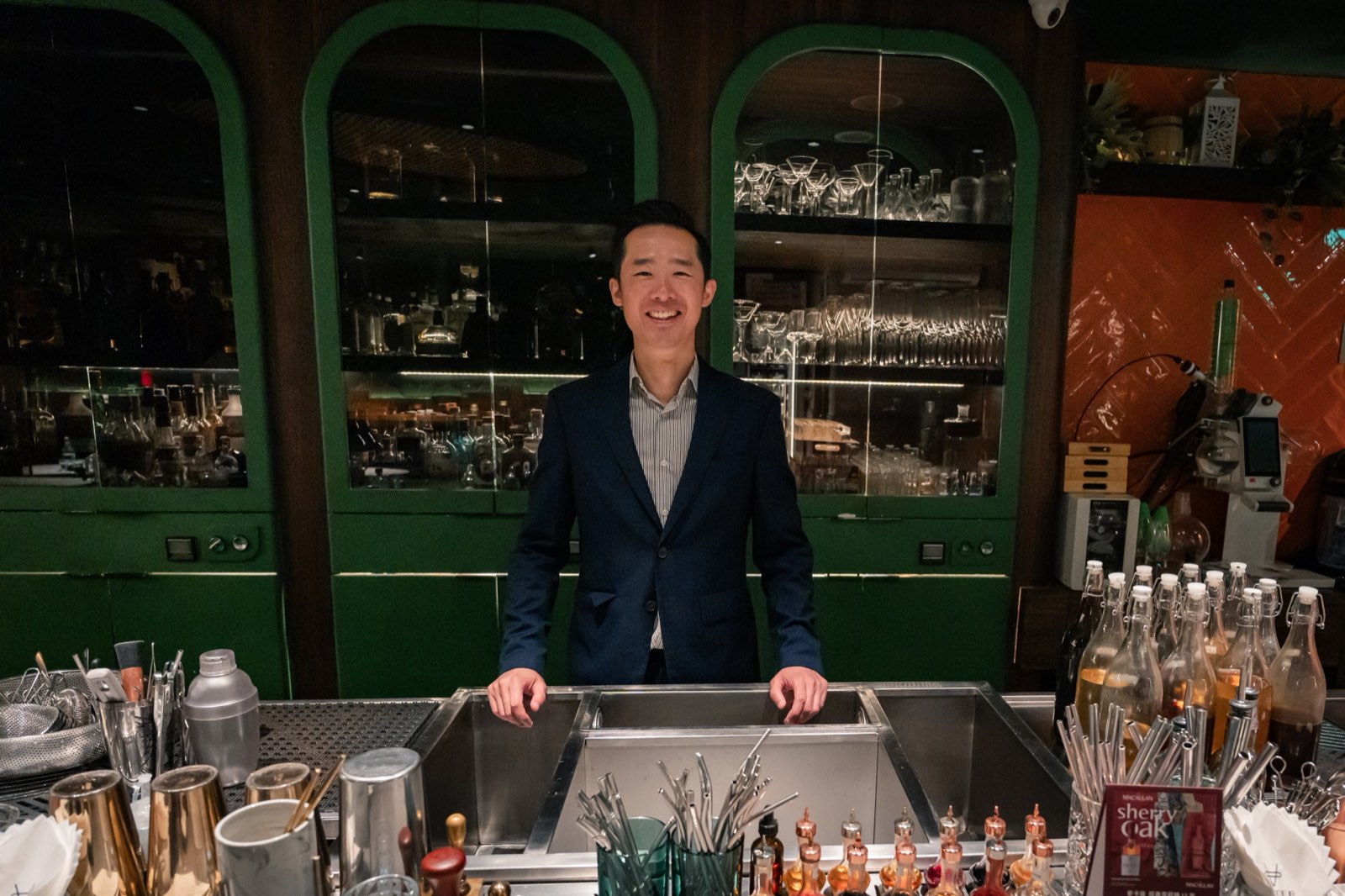 Darren 站在 Vender 吧檯後方，身後是綠色拱形酒櫃