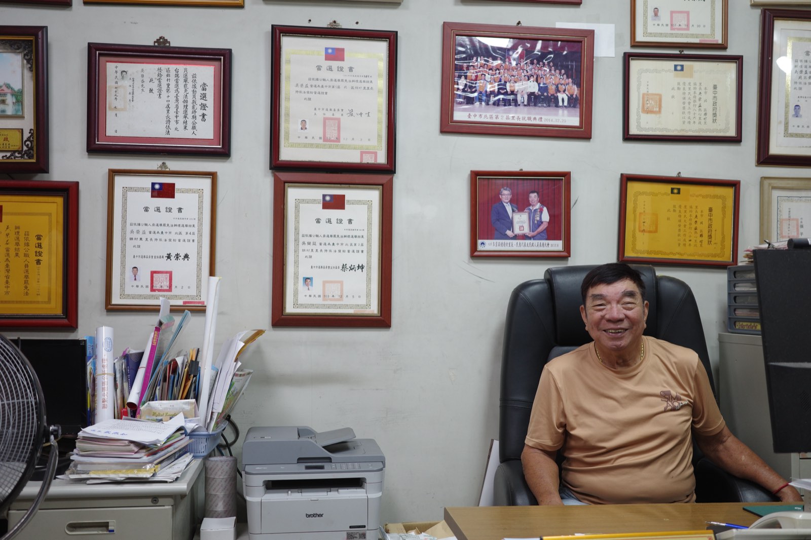吳榮益坐在辦公室裡，身後牆上掛滿獎狀與照片