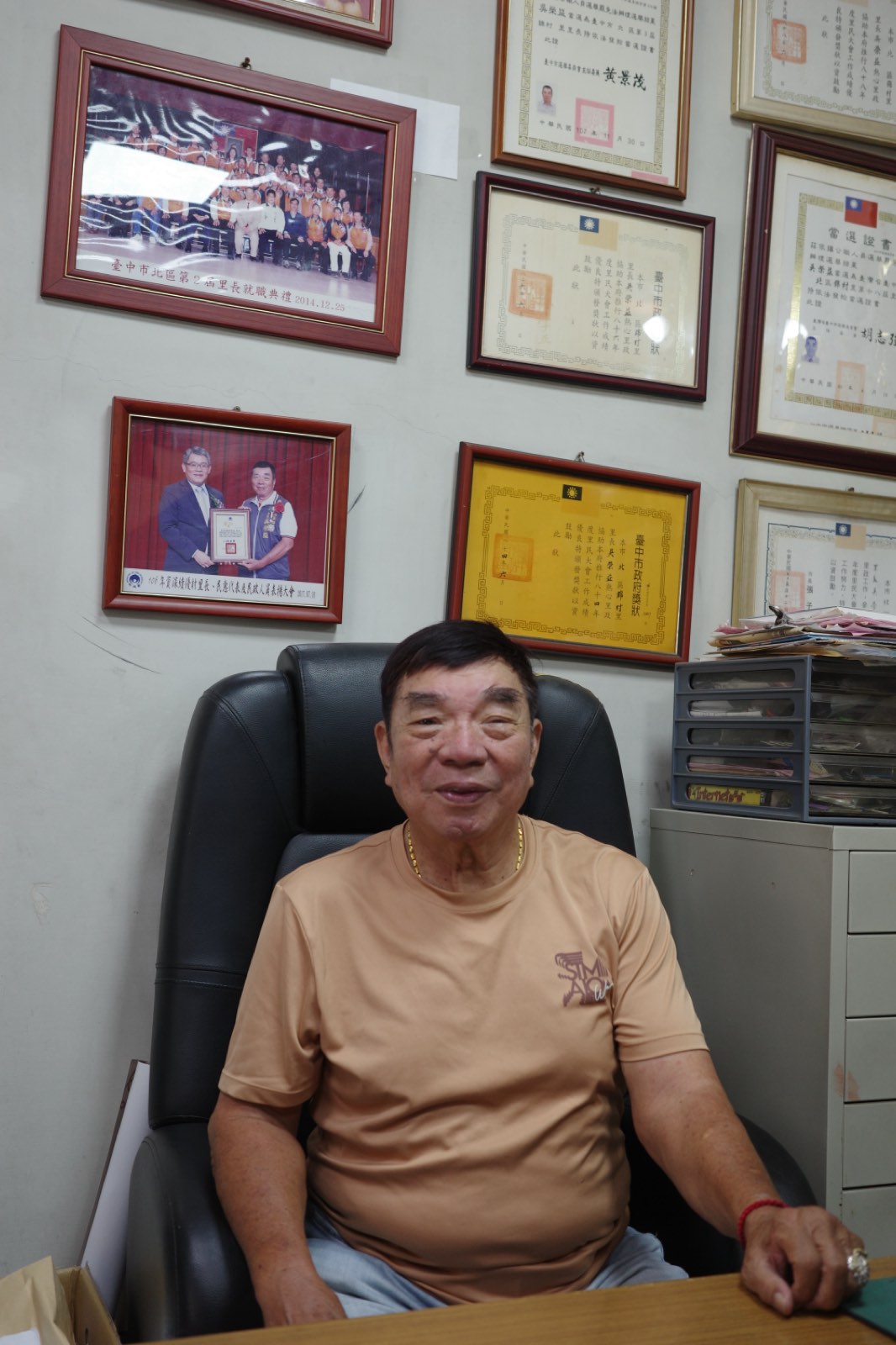 吳榮益坐在辦公室皮椅上微笑，身後是滿牆的獎狀
